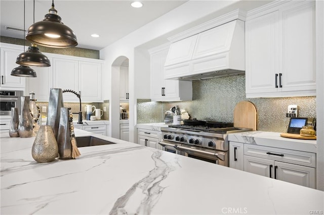 kitchen featuring white cabinets, appliances with stainless steel finishes, hanging light fixtures, arched walkways, and premium range hood