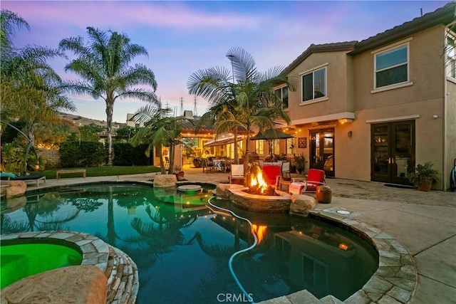pool at dusk featuring a patio, an outdoor fire pit, and a pool with connected hot tub