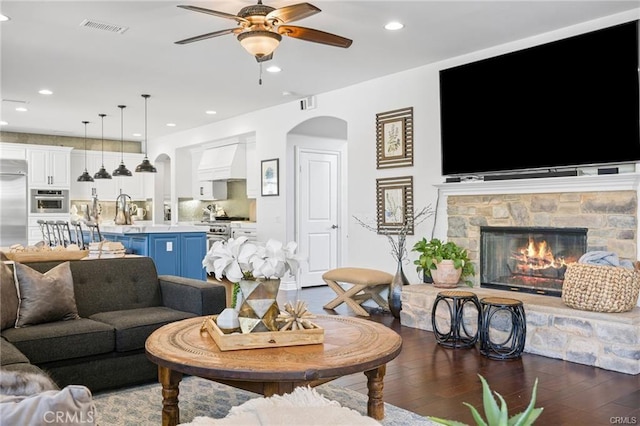living room featuring visible vents, a ceiling fan, wood finished floors, a fireplace, and arched walkways