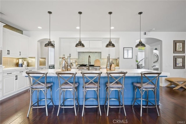 kitchen with dark wood-type flooring, light countertops, white cabinets, tasteful backsplash, and arched walkways