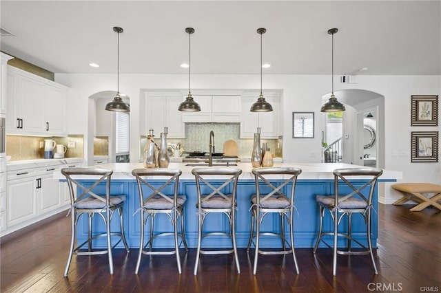 29291 Via Zamora, San Juan Capistrano, CA 92675 - kitchen featuring arched walkways, backsplash, dark wood-style floors, light countertops, and white cabinets
