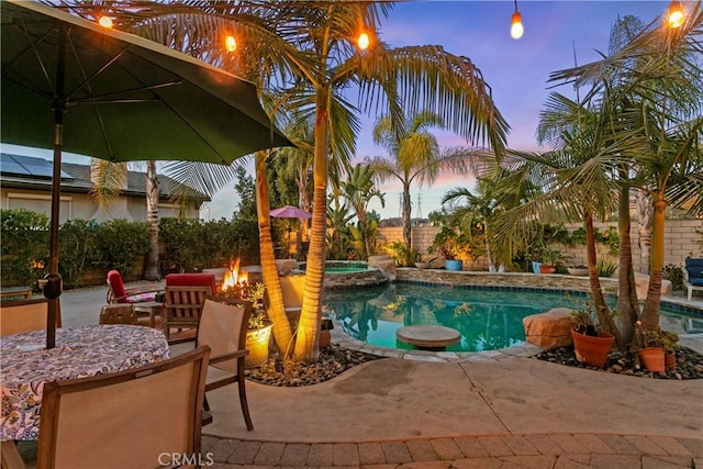 pool at dusk with a fenced backyard, a pool with connected hot tub, an outdoor fire pit, and a patio area