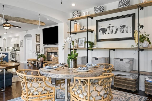 dining area with ceiling fan, arched walkways, wood finished floors, a glass covered fireplace, and recessed lighting