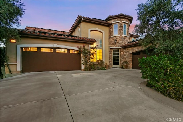mediterranean / spanish house with a garage, stone siding, and concrete driveway