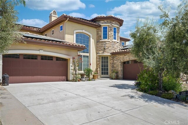 mediterranean / spanish-style home featuring stone siding, stucco siding, driveway, a tile roof, and solar panels