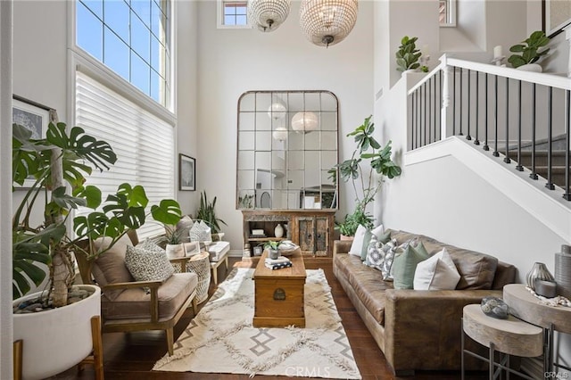 living area with stairs, a notable chandelier, wood finished floors, and a towering ceiling
