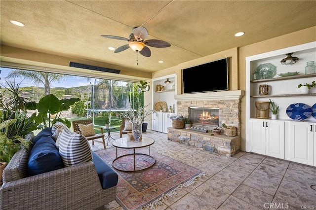 living room featuring a ceiling fan, a textured ceiling, built in shelves, an outdoor stone fireplace, and recessed lighting