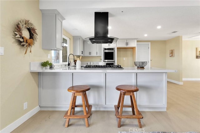 kitchen with light wood-style floors, a peninsula, baseboards, stainless steel appliances, and island range hood