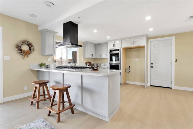 kitchen featuring appliances with stainless steel finishes, light wood-style flooring, a peninsula, baseboards, and island range hood