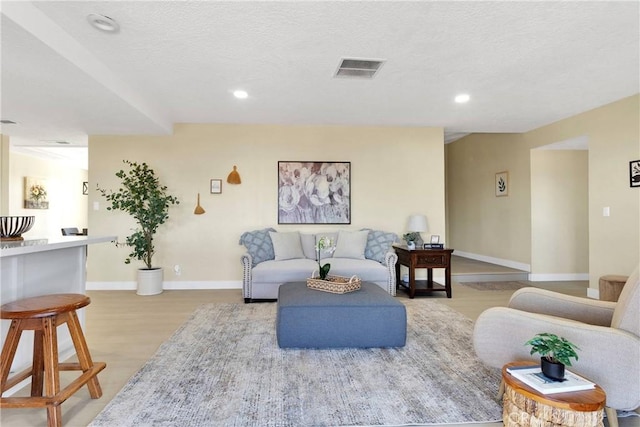 living room with light wood finished floors, a textured ceiling, recessed lighting, baseboards, and visible vents
