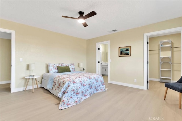 bedroom with baseboards, a walk in closet, light wood-style flooring, and visible vents