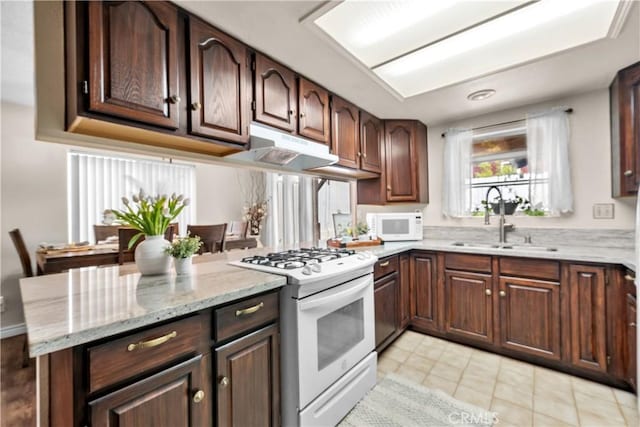 kitchen with light stone counters, a sink, white appliances, light tile patterned floors, and under cabinet range hood