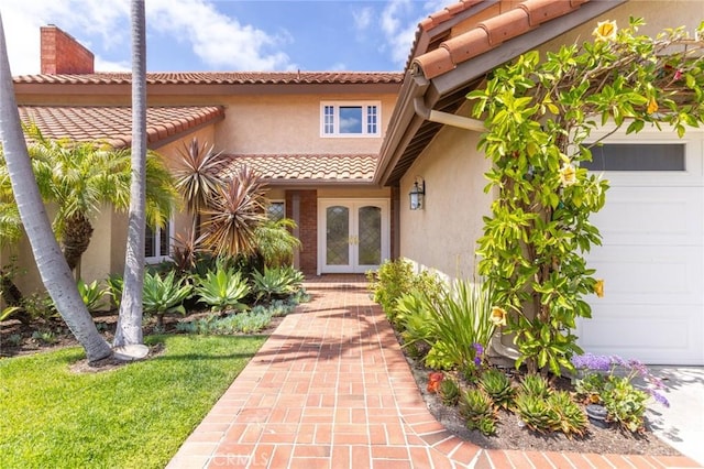 view of exterior entry with an attached garage, stucco siding, french doors, and a tiled roof