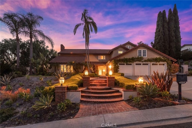 view of front facade featuring a garage, stucco siding, a chimney, a tiled roof, and driveway