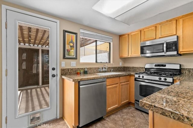 kitchen featuring stainless steel appliances, dark countertops, light tile patterned floors, and a sink