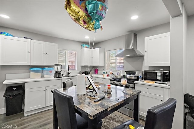 kitchen with light countertops, white cabinets, light wood finished floors, stainless steel appliances, and wall chimney exhaust hood