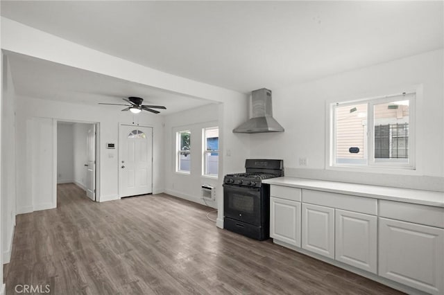 kitchen featuring wall chimney range hood, a ceiling fan, dark wood-style flooring, light countertops, and black range with gas stovetop