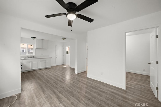 unfurnished living room featuring baseboards, a sink, ceiling fan, and wood finished floors