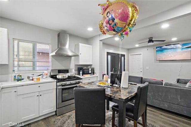 kitchen featuring wall chimney range hood, wood finished floors, gas stove, white cabinets, and recessed lighting