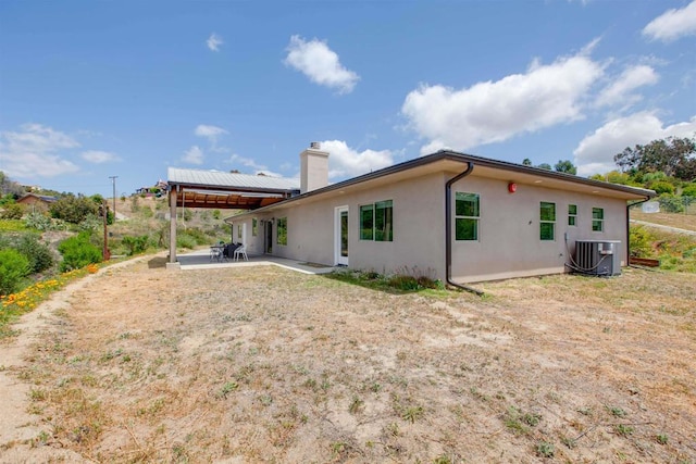 back of property with central AC unit, a chimney, a patio area, and stucco siding