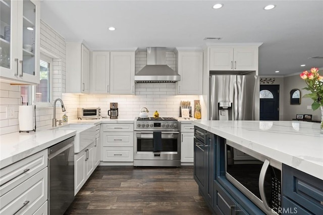 kitchen featuring light stone counters, white cabinetry, wall chimney range hood, and stainless steel appliances