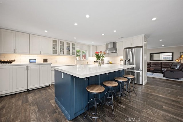 kitchen featuring wall chimney range hood, stainless steel fridge, dark wood-type flooring, white cabinetry, and backsplash