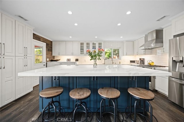 kitchen featuring wall chimney range hood, white cabinets, appliances with stainless steel finishes, and visible vents