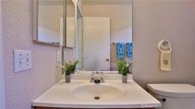 half bathroom featuring vanity, a textured wall, and toilet