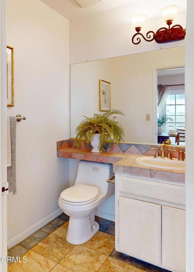 bathroom featuring toilet, baseboards, stone finish flooring, and vanity