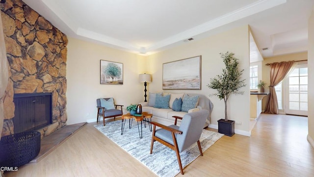 living room featuring visible vents, light wood-style flooring, a tray ceiling, and a stone fireplace