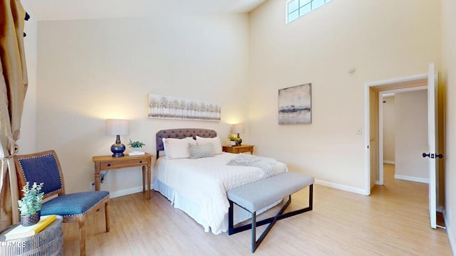 bedroom featuring a towering ceiling, baseboards, and light wood-type flooring