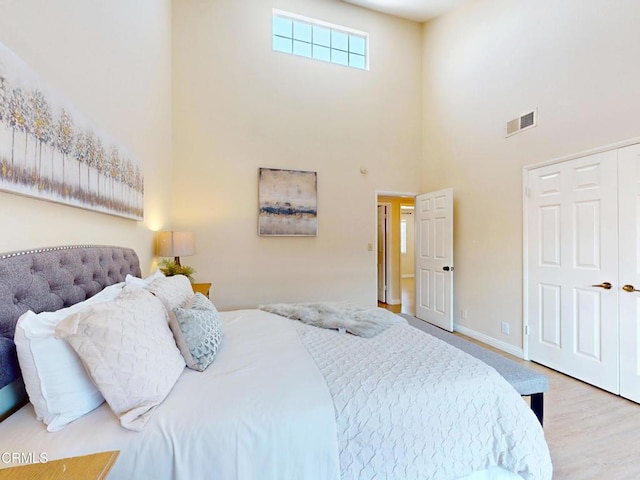 bedroom with visible vents, a closet, wood finished floors, baseboards, and a high ceiling
