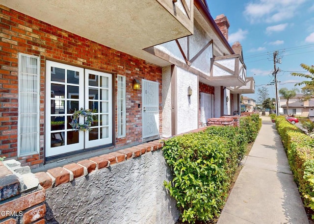 view of property exterior featuring brick siding, stucco siding, french doors, and a chimney