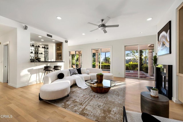 living room featuring a glass covered fireplace, a bar, a ceiling fan, and light wood-style flooring