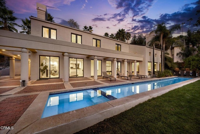 rear view of property featuring stucco siding, a pool with connected hot tub, a patio area, and a chimney