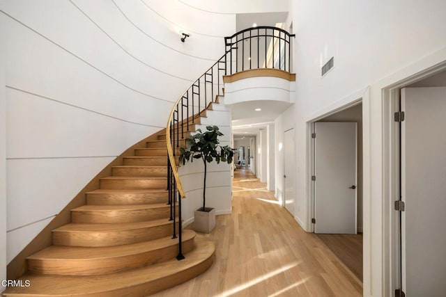 stairway with a high ceiling, wood finished floors, and visible vents