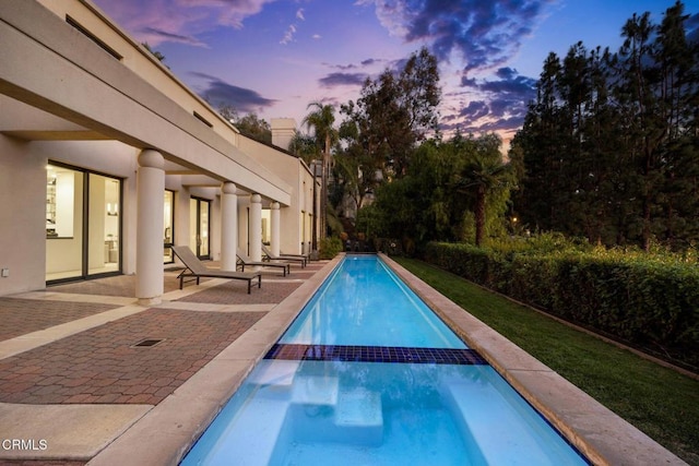 pool at dusk featuring a patio and a pool with connected hot tub