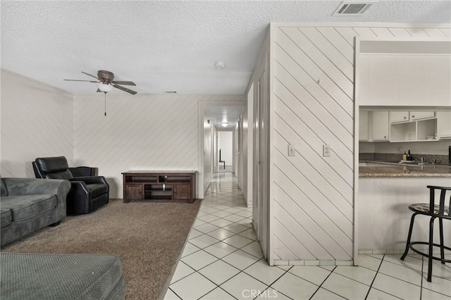 living area with light tile patterned floors, a ceiling fan, a textured ceiling, and visible vents