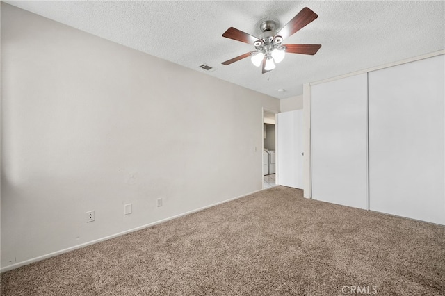 unfurnished bedroom featuring a textured ceiling, carpet, visible vents, washing machine and dryer, and a closet