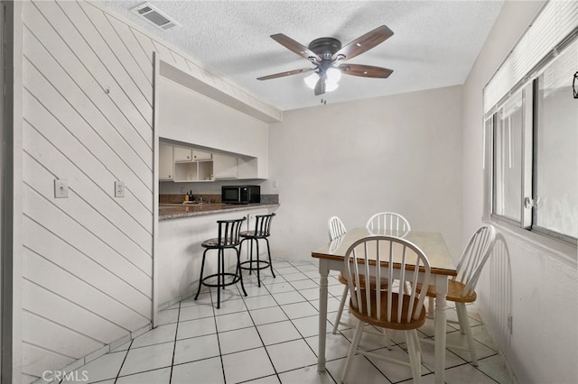 dining space with visible vents, a ceiling fan, a textured ceiling, and light tile patterned floors
