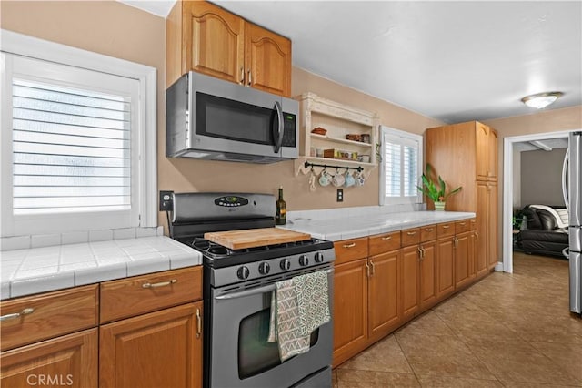 kitchen with light tile patterned floors, appliances with stainless steel finishes, tile countertops, and brown cabinets