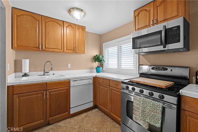 kitchen with a sink, light tile patterned floors, brown cabinets, and stainless steel appliances