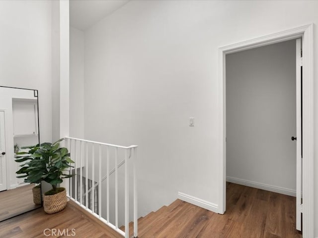 hallway featuring baseboards, an upstairs landing, and wood finished floors