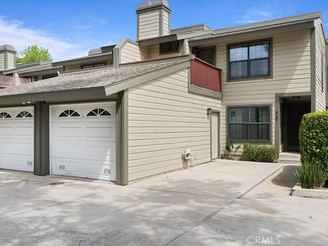 view of property exterior with concrete driveway, a chimney, and a balcony