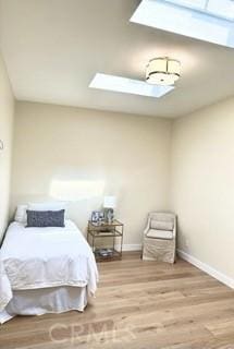bedroom with baseboards, wood finished floors, and a skylight