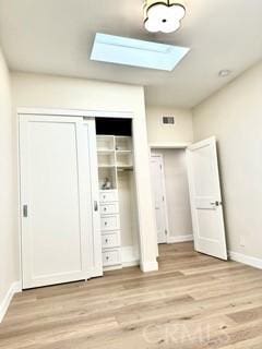 unfurnished bedroom with a closet, light wood finished floors, baseboards, and a skylight