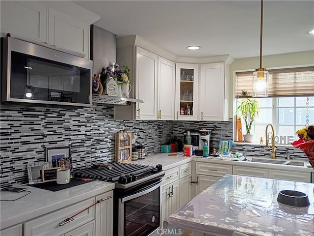kitchen featuring glass insert cabinets, white cabinets, tasteful backsplash, a sink, and stainless steel appliances