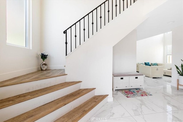 stairway with a healthy amount of sunlight, a towering ceiling, baseboards, and marble finish floor