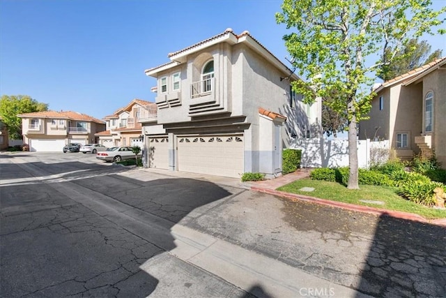 view of front of house with a garage, fence, stucco siding, a tiled roof, and a residential view