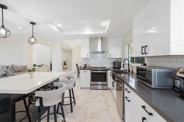 kitchen featuring modern cabinets, wall chimney range hood, white cabinets, a sink, and stainless steel appliances